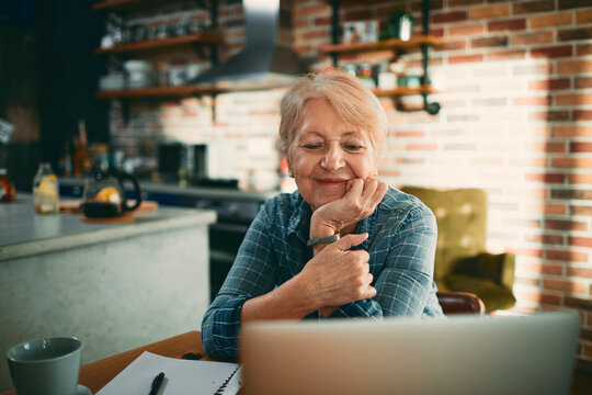 Smiling senior woman using laptop at home kitchen table