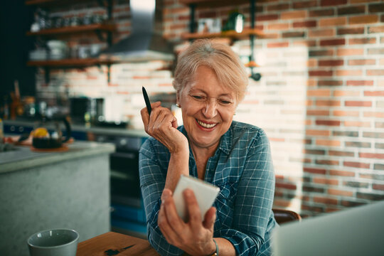 Smiling senior woman using smartphone in home kitchen