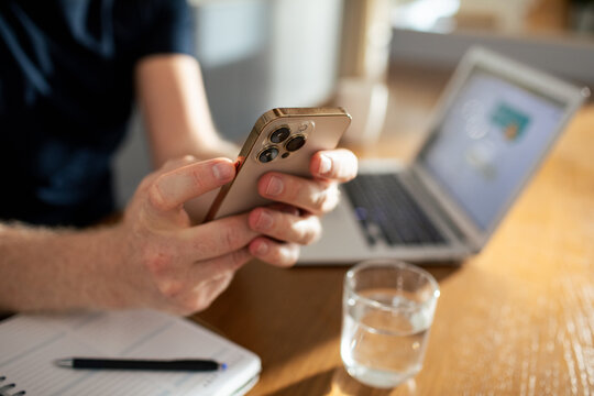 Person using smartphone with laptop at home office desk