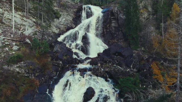 Aerial shot with camera rising up along a waterfall flowing down a rocky cliff