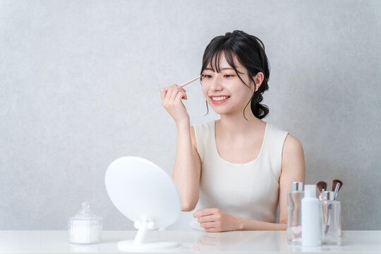 A young Asian woman applying eyeshadow while doing her makeup.