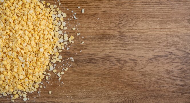 Wood tabletop bearing a heap of milled corn kernels intended for porridge and crisp flakes