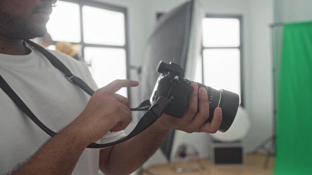 Man adjusts camera dials and holds the lens while checking settings next to softbox and greenscreen in a studio; focused concentration.