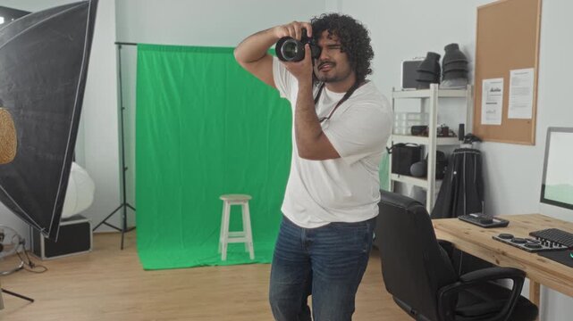 Man holding camera with hand raised to frame shot, looking through viewfinder in studio; creative concentration.