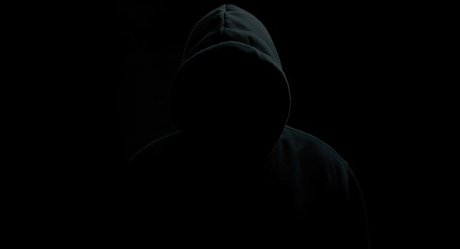 Unknown hacker identity in a shadowy hood figure creating scary Halloween mood copy space