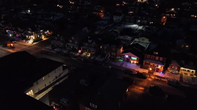 Aerial night view of Pennsylvania neighborhood decorated with colorful Christmas lights, showing festive homes, quiet streets and warm holiday atmosphere in suburban winter setting. Approaching shot