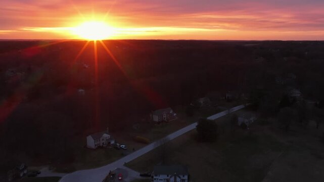 Aerial sunset over rural suburban neighborhood in United States with sun rays, single family homes and quiet cul de sac street. Peaceful spring evening landscape of American residential area.