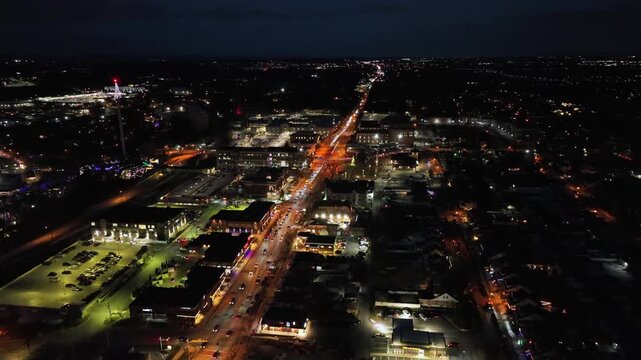 Aerial night view of an illuminated American town main street with traffic, glowing city lights and festive Christmas atmosphere, with busy roads and small-town urban layout in USA. Hershey, PA. Wide.