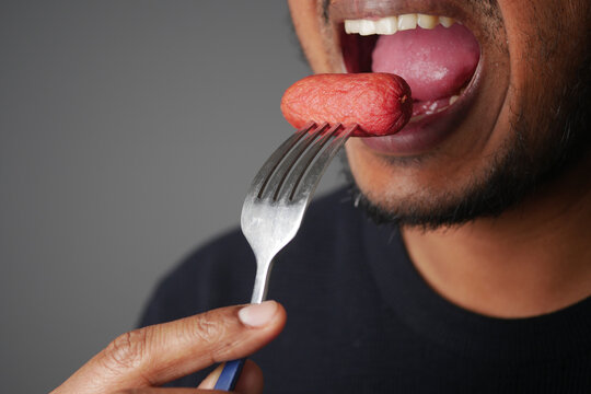 Close-Up Man Eating Sausage On Fork Showing Mouth, Tongue And Hand