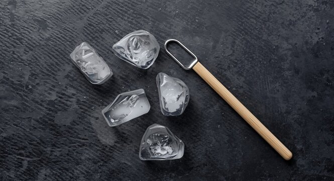 Still life setup featuring ice cubes and a wooden handled ice pick against a dark textured background