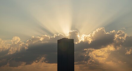 Obraz premium Sunlight penetrating cloud layers creating a glowing effect on skyscraper