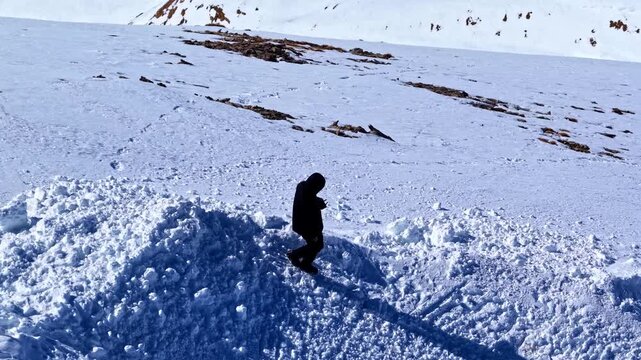 Person standing on snow covered alpine ridge with mountain slopes in Serfaus Fiss Ladis Austria, aerial tilt down follows as they walk