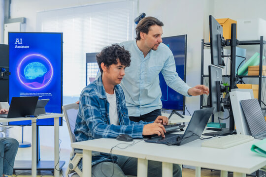 Caucasian mentor pointing at laptop screen while coaching young programmer in modern tech office, perfectly capturing teamwork, IT training, software development, and knowledge transfer.