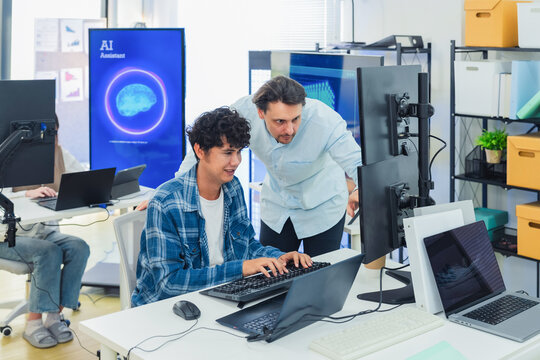 Caucasian mentor pointing at laptop screen while coaching young programmer in modern tech office, perfectly capturing teamwork, IT training, software development, and knowledge transfer.