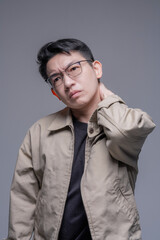 Obraz premium Asian man with glasses suffering from shoulder pain or muscle stiffness, touching his joint in discomfort against a grey studio background for health and medical concepts.