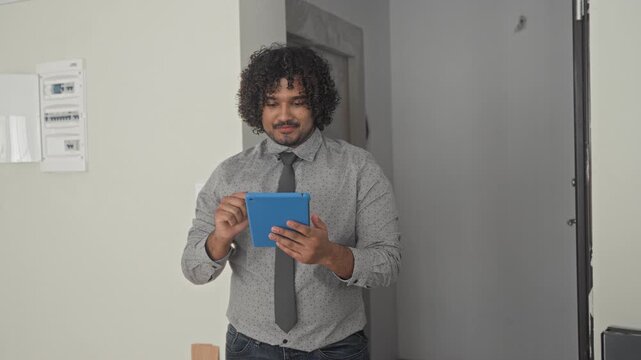 Man tapping blue tablet with hands inside a building during an empty house walkthrough; confidence property viewing.
