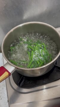 Freshly cut green long beans are dropped into the pot of boiling broth, mixing with the previously added shallot.
