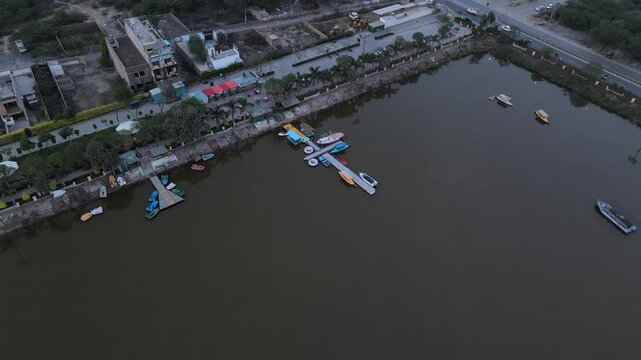 Boats docked at a pier on a lake with industrial background and hazy sky.