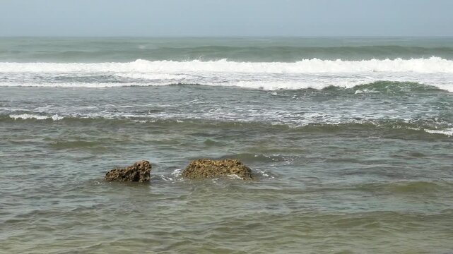 4K scenic view of ocean waves breaking in the distance with rocks in shallow water foreground