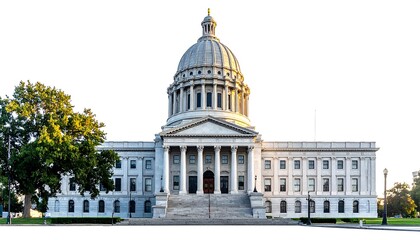 Naklejka premium A neoclassical building with a large dome stands centered, flanked by trees and a clear sky background. The structure features steps and columns