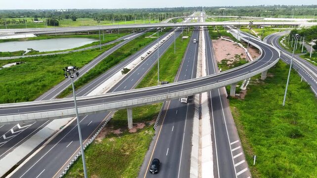Aerial view of modern highway interchange with multilayer roads and curved ramps surrounded by green farmland, showcasing transportation infrastructure, urban development, and road network planning.