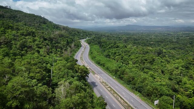 High-angle drone footage of a winding mountain road cutting through dense green forest, capturing natural landscape, scenic travel route, and peaceful countryside environment from above.