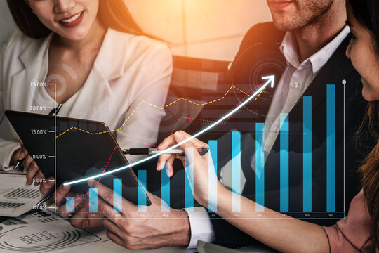 Two business professionals interact in a modern office discussing financial data with a digital tablet and visual graphs, symbolizing teamwork and growth. Scalp
