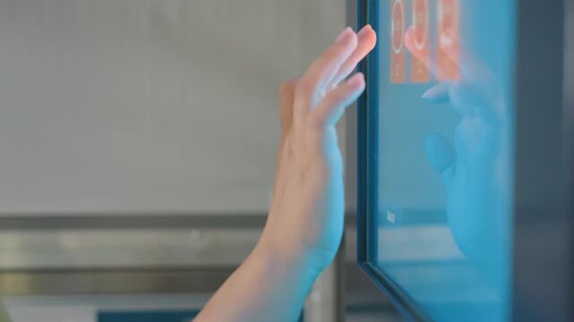 Close up female hands reach to payment kiosk screen inside laundromat, tapping icons, blue glow on fingers, contactless self service interface, cashless transaction, technology