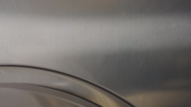 Downward view shows machine indicator above stainless panel while fabric spins inside washing machine drum, soapy water clings to glass, bubbles streak surface, modern laundromat vibe