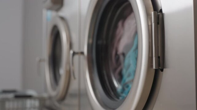 Close up components of washing machine row showing doors and handles, inner view revealing clothes soaking in bubbling water, detailed focus on stainless finish and laundry process inside laundromat