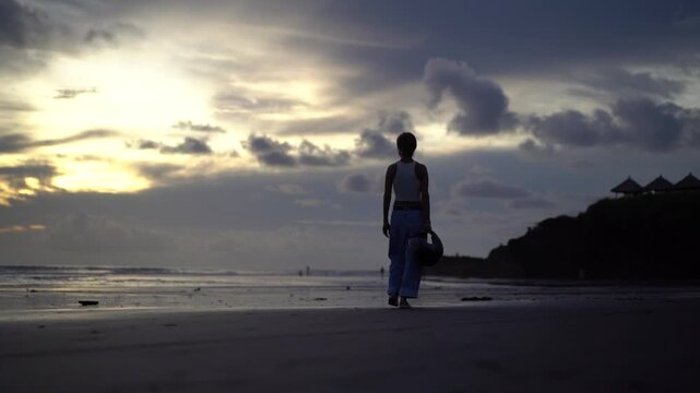 Woman Silhouette Walking Away on Beach Holding Helmet