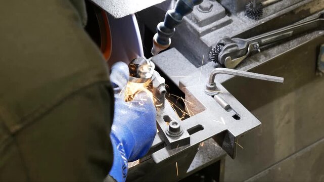 Worker uses a manual grinding machine to sharpen a metal tool bit
