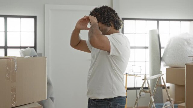 Man with cardboard box and bubblewrap removes face mask while unpacking boxes and smiles in a building; relief fresh start.