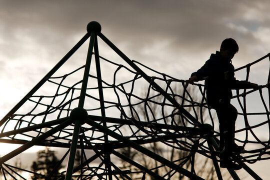 Silhouette of a young boy climbing on a rope playground at dusk