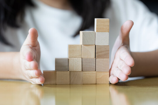 oth hands hold a wooden block tower as small fingers slowly adjust and place pieces one by one on a rug keeping the structure upright neat and stable through careful practice.