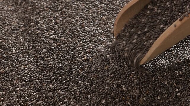 close up of chia seeds pours out of a wooden scoop food texture and background