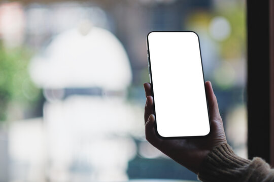 Mockup image of a woman holding and using mobile phone with blank desktop screen