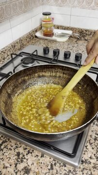 Chef cooking sofrito with fried onions and garlic in a pan on a gas stove