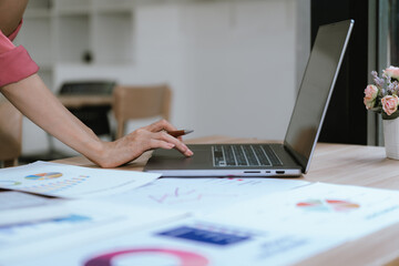 Fototapeta premium A professional reviews financial reports, pointing at charts while working on a laptop, analyzing data and planning business strategy at a modern office desk.