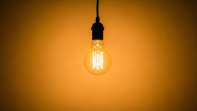 Retro incandescent light bulb emitting a warm amber glow on orange background