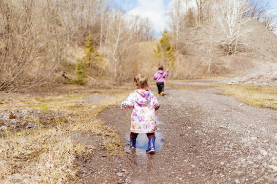 Siblings running through fresh muddy puddles after spring rain