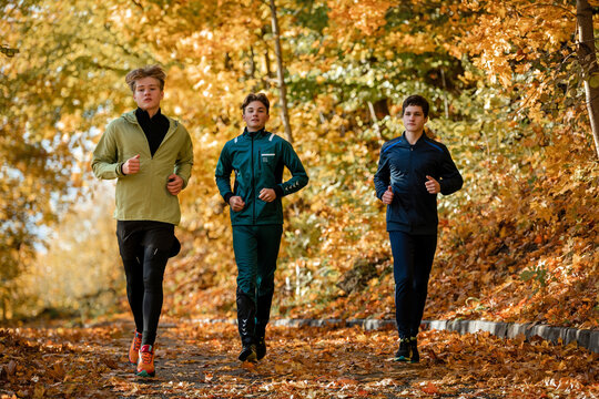 Three teenage boy athlete jogging through autumn park.