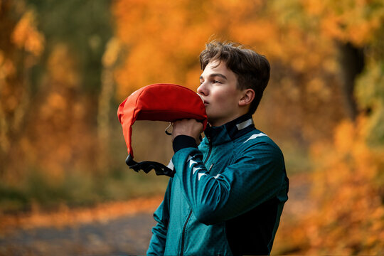 Teen boy drinking from hydration pack while running in autumn