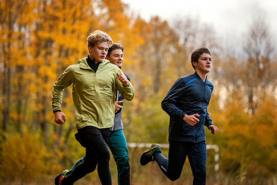 Group of teenage boy runners jogging along a path in autumn forest.