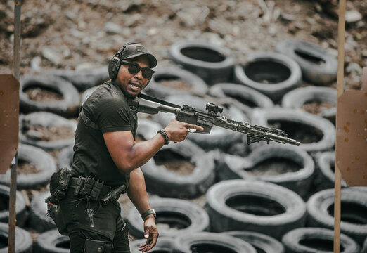 Man holding a rifle during tactical training in front of stacked tires