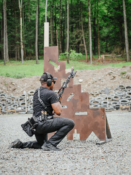 Man aiming a rifle beside a brown barricade at an outdoor range