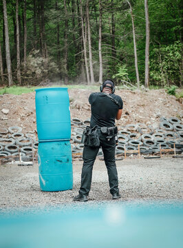 Man aiming a handgun behind blue barrels at an outdoor range