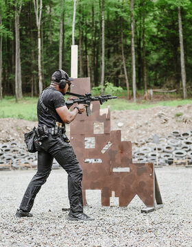 Man aiming a rifle beside a brown barricade at an outdoor range