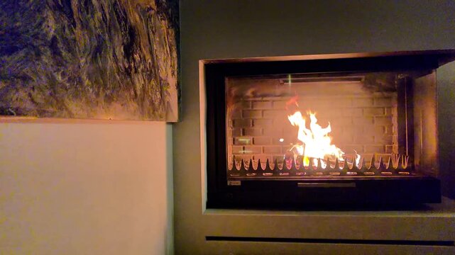 Modern indoor fireplace with glowing flame in brick enclosure, set against smooth neutral wall and abstract artwork, creating cozy warmth and stylish contemporary ambiance