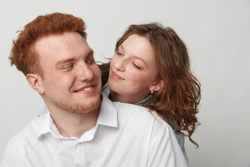 Obraz premium Happy young couple with red hair and curly hair smiling and looking at each other on white background. Concept of love, relationship, friendship, and positive emotions between people.